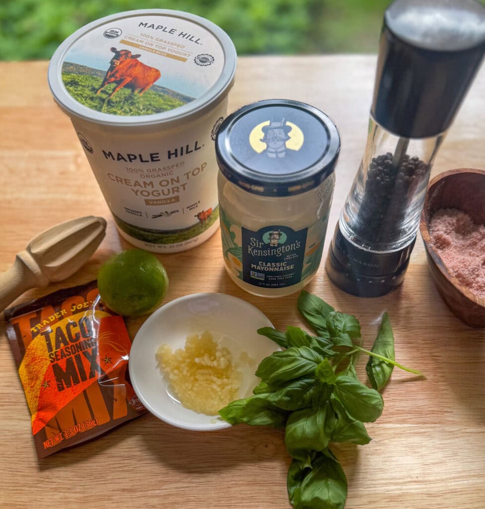 creamy taco salad dressing ingredients with yogurt, mayo, lime, garlic and basil on a wooden board