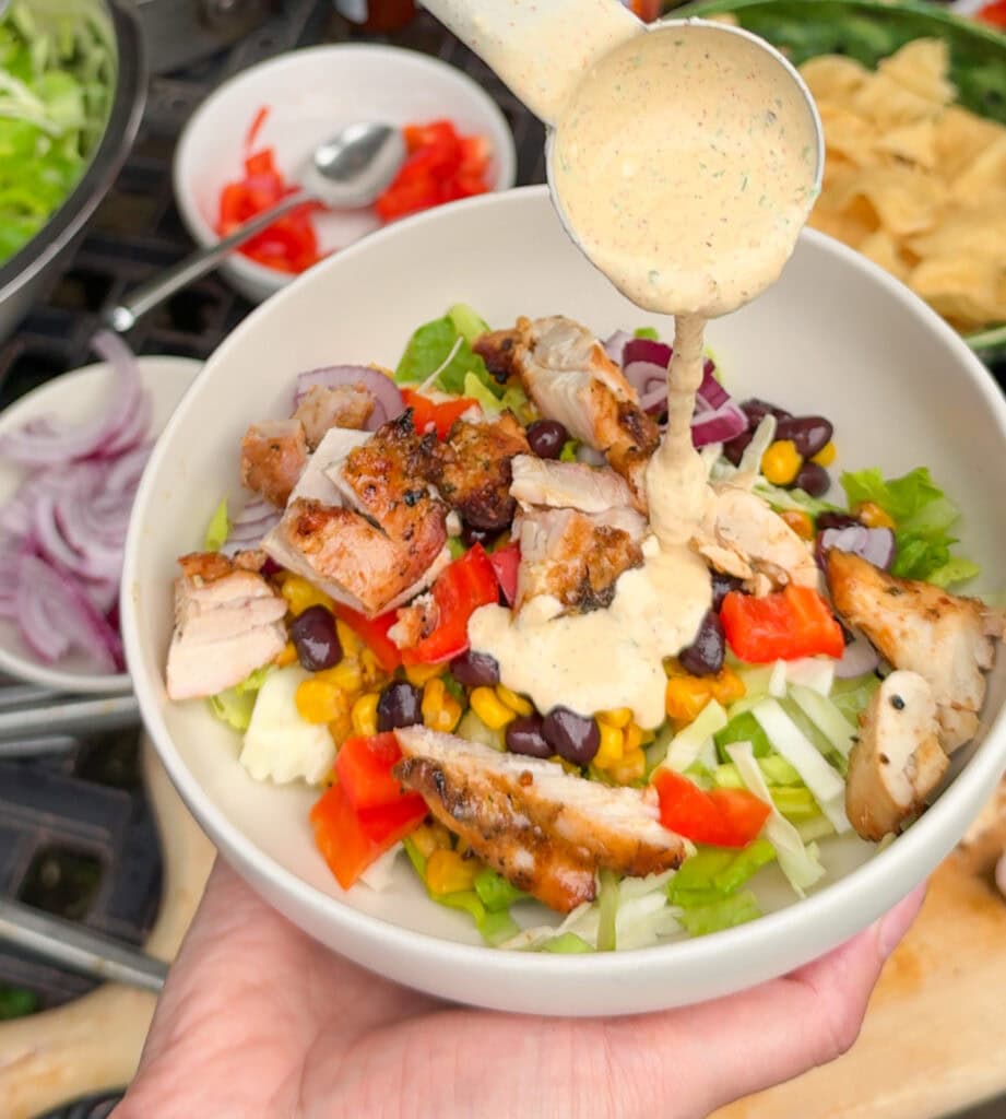 taco salad with grilled chicken and creamy taco salad dressing being poured on top