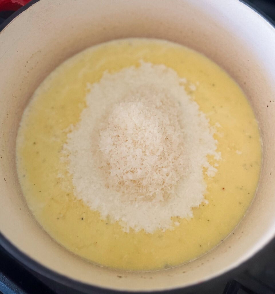 adding grated parmesan cheese to creamy alfredo sauce in a pot