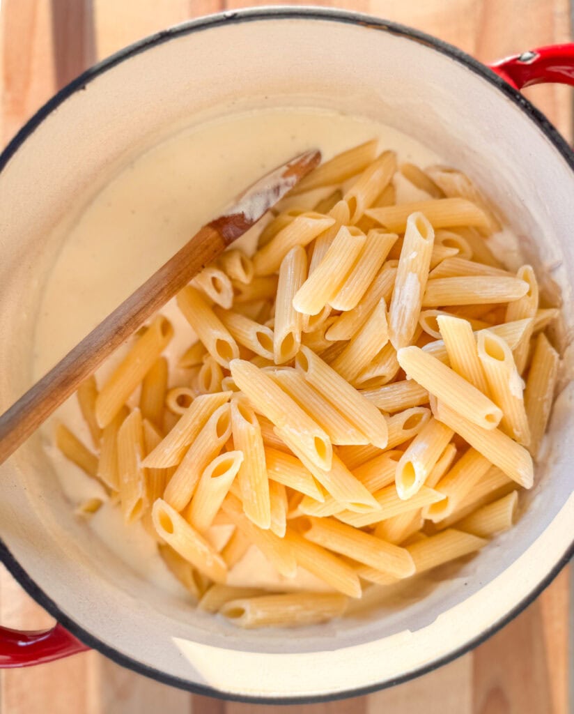 penne pasta added to creamy garlic alfredo sauce in a pan