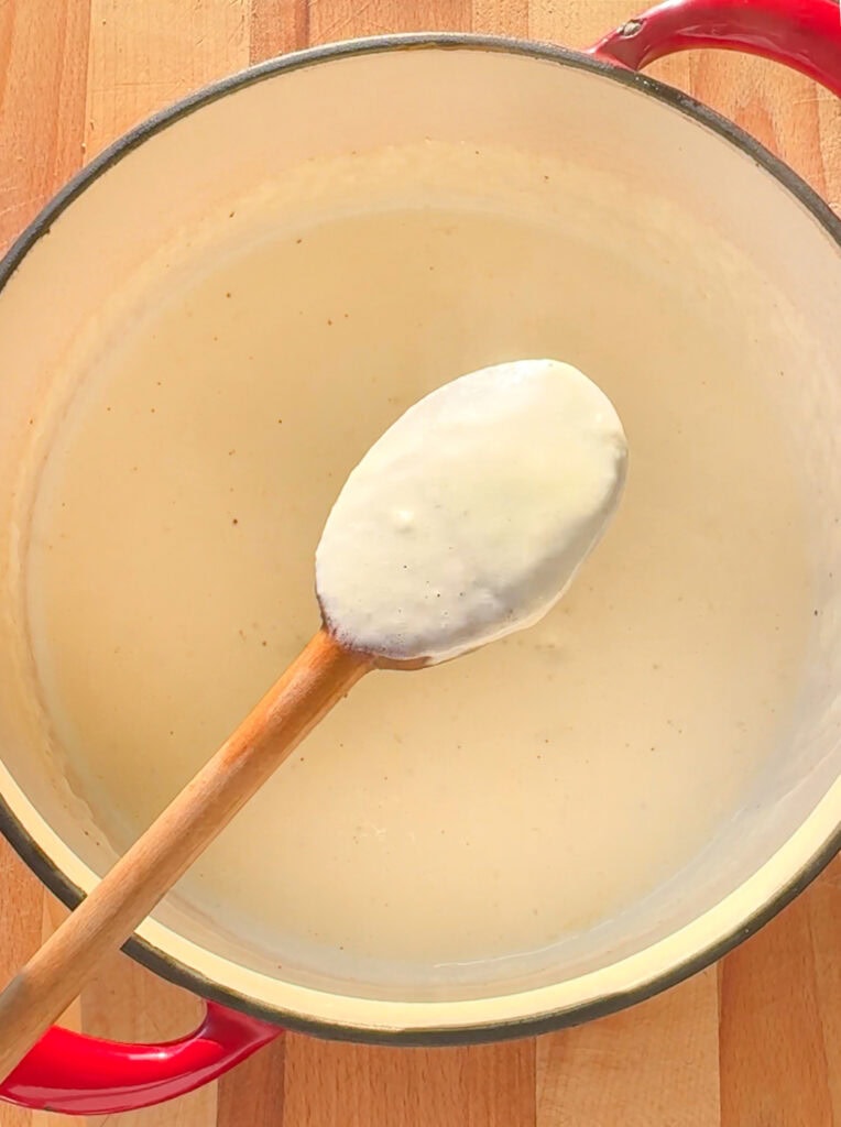 Creamy garlic alfredo sauce in a pan with a spoon, smooth and thick texture