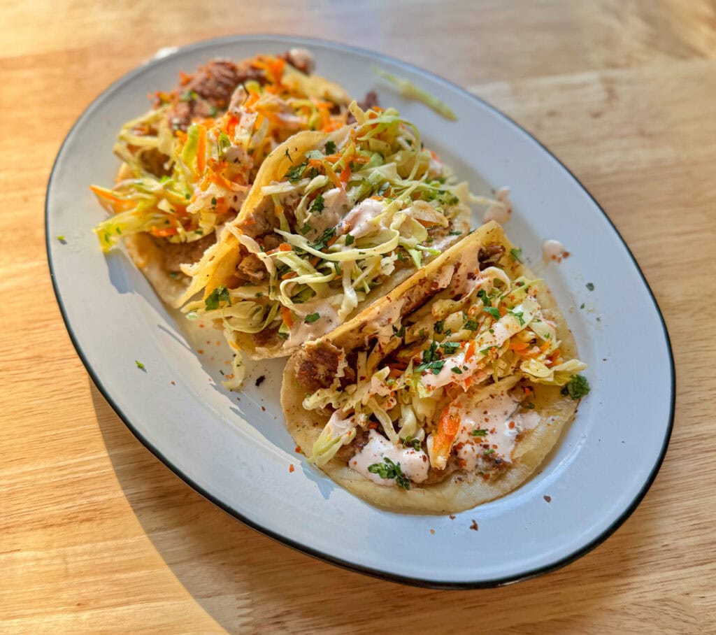 Crispy Asian smash tacos topped with crunchy cabbage slaw, spicy mayo, scallions, and sesame seeds on a blue plate.