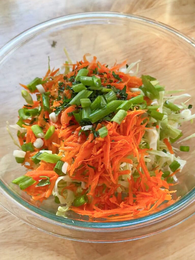 Shredded cabbage, carrots, and scallions in a glass bowl for Asian smash taco slaw.