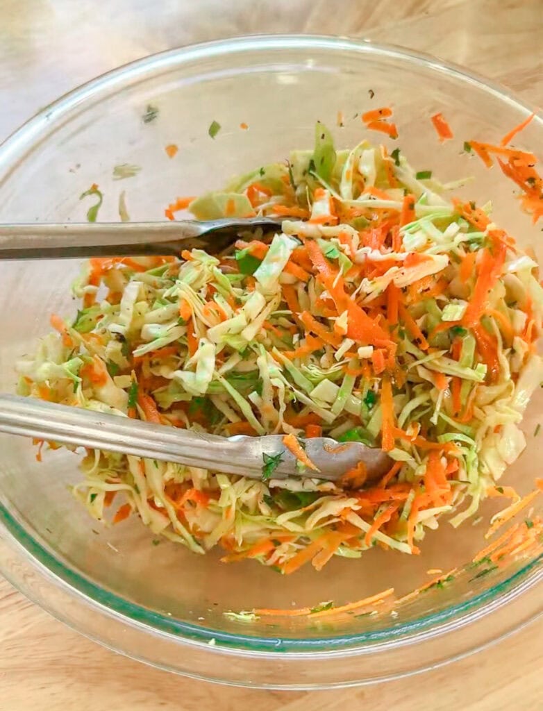 Crunchy cabbage slaw with shredded carrots and scallions in a glass bowl.