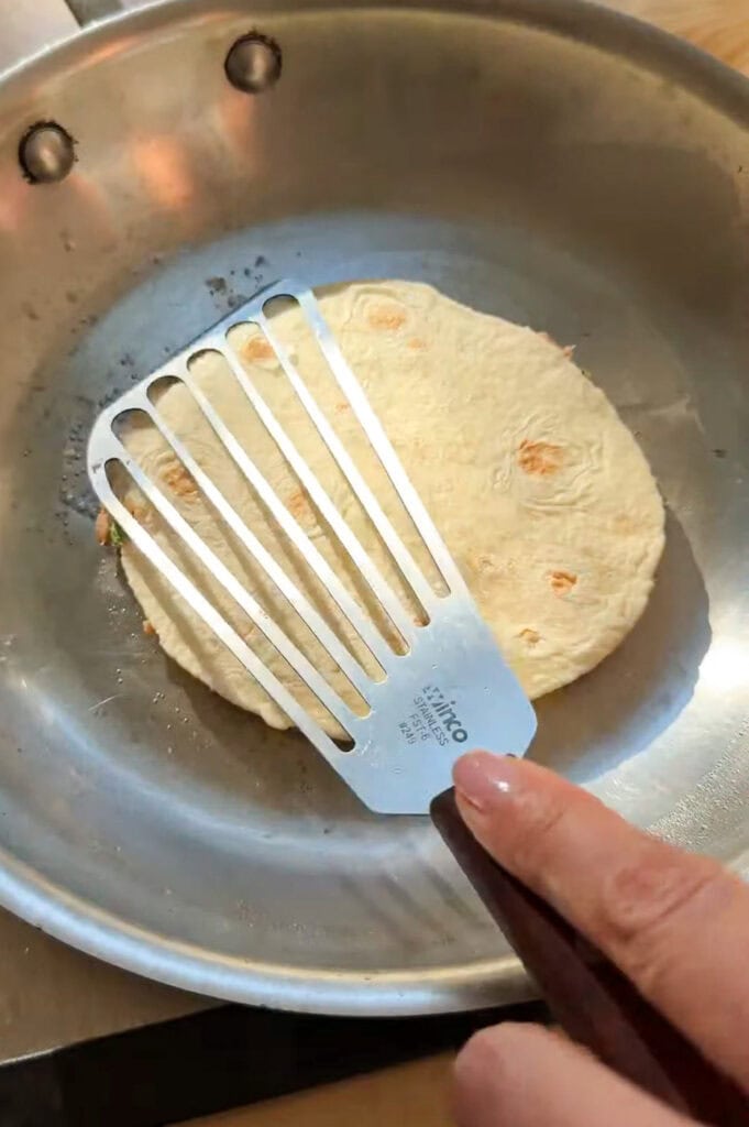 Small tortilla being pressed into a hot skillet with a spatula for crispy smash tacos.