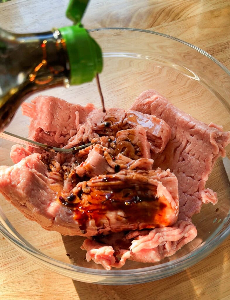 Soy sauce being poured over ground turkey in a glass bowl for Asian smash tacos.